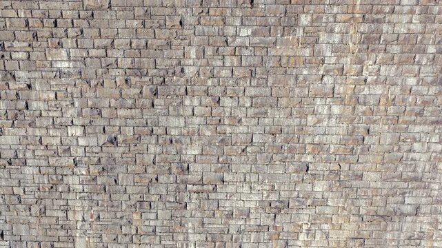 Aerial video showcasing the gritstone masonry crest of Derwent Dam, slowly revealing the expansive, deep blue waters of Derwent Reservoir in Derbyshire, UK. 