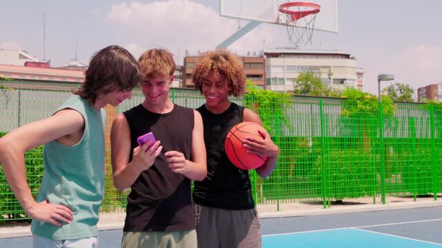 Young multicultural male friends watching a smartphone on a basketball court