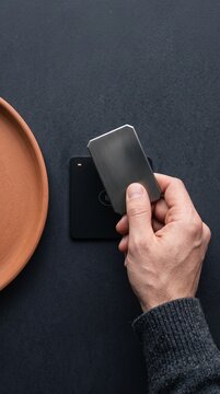 Close-up of a customer paying with a modern metal contactless credit card on a sleek pos terminal over a dark textured table