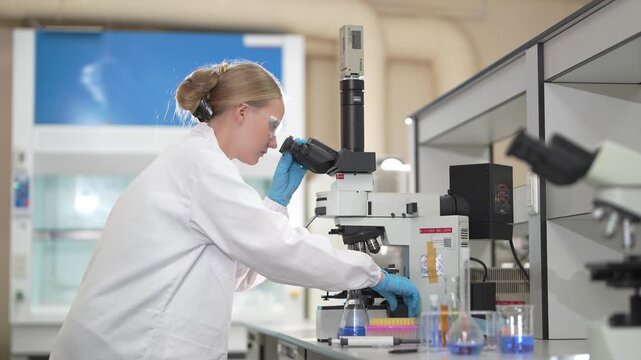 Scientist in a white lab coat using a microscope for research in a modern clinical laboratory