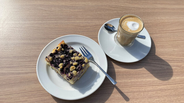 blueberry crumble cake and cafe cortado on outdoor coffee table in harsh sunlight with strong shadows