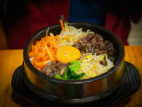 Korean popular meal Dolsot Bibimbap, translated as stone pot mixed rice, served in a sizzling hot stone bowl with vegetables, a fried egg on top, and a delicious crispy layer of rice at the bottom.