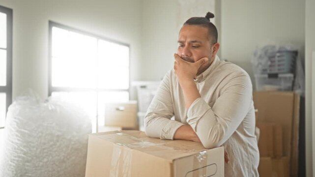 Man leaning on sealed moving box, hand on chin with eyes closed in building filled with stacked packages; contemplation transition.