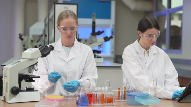 Two female scientists working with pipettes and microscopes in a modern laboratory environment