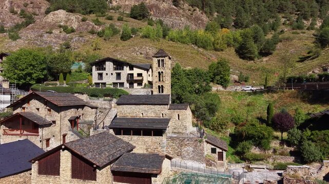 Aerial view of the Romanesque Church of Sant Climent de Pal and its three-storey Lombard bell tower surrounded by stone village buildings and forested mountain slopes, Pal, Andorra