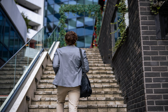 Back view of young businessman walking up outdoor stairs in city business district