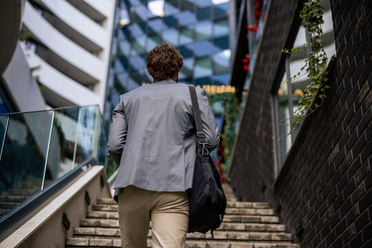 Rear view close up of young businessman carrying shoulder bag walking up stairs