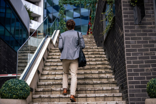 Back view of professional man with bag climbing stairs in modern urban environment