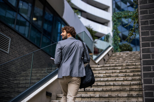 Rear view of businessman turning around while walking up stairs in business district