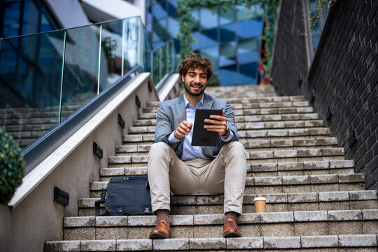 Full body view of businessman sitting on outdoor stairs using digital tablet