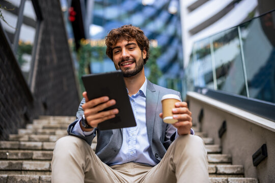 Young businessman with coffee using digital tablet outdoors on stairs