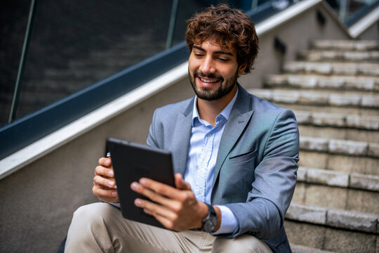 Corporate worker smiling while reading on digital tablet on outdoor stairs