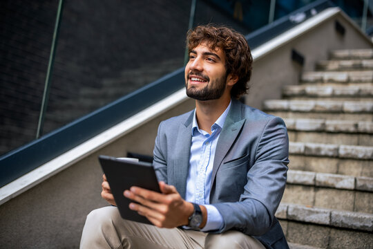 Businessman looking up thoughtfully while holding digital tablet on outdoor stairs