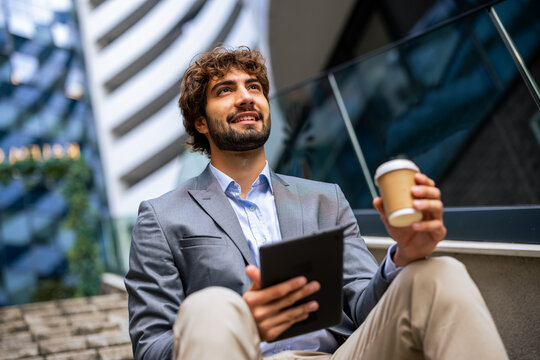 Low angle portrait of businessman holding tablet and coffee looking up outdoors