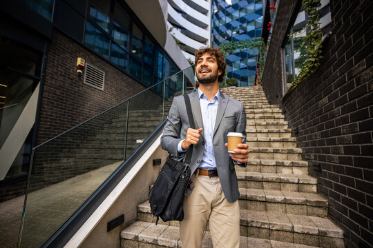 Low angle view of young businessman walking down stairs holding coffee cup