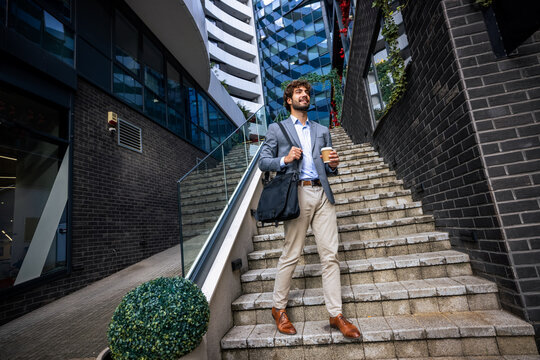 Full body low angle shot of businessman with coffee walking on outdoor stairs