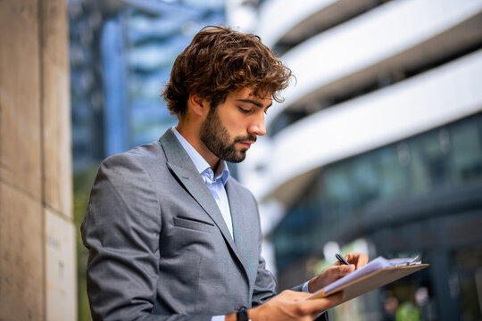 Young professional man writing on clipboard in urban office district