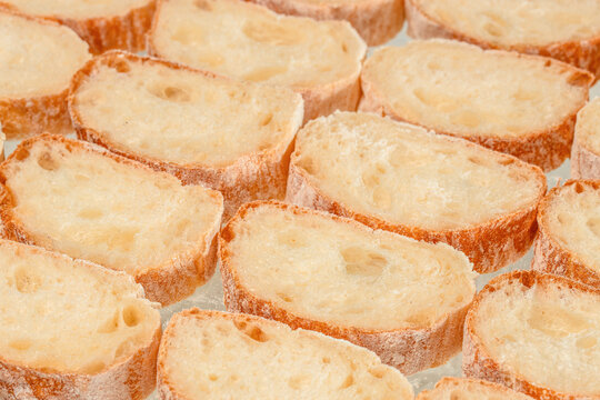 Sliced toasted baguette pieces arranged in a close overhead food texture with golden crusts, pale porous interiors, and rustic bread surfaces filling the frame