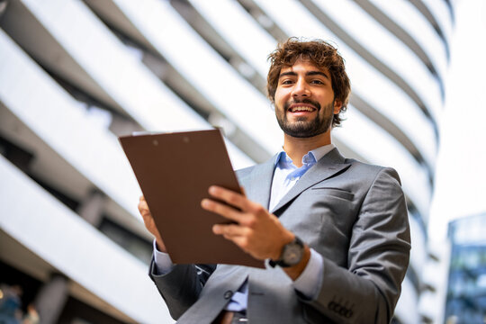 Smiling businessman holding clipboard in modern office district