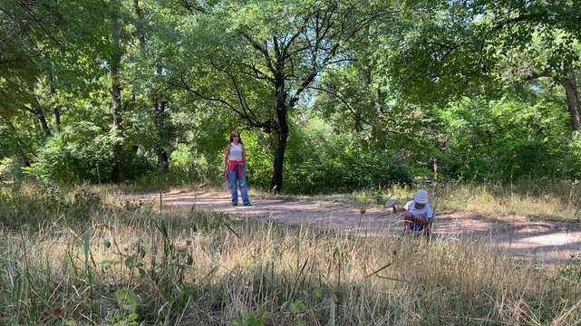A loving mother and her active young son play badminton. The eager boy prepares to hit a shuttlecock on a path in a green forest. They share a joyful and peaceful moment.
