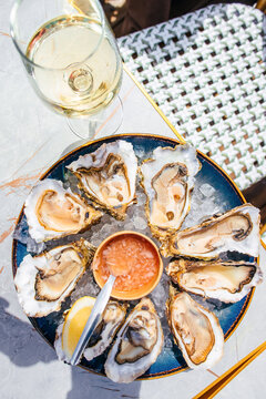 Top view of fresh oysters on crushed ice with citrus dipping sauce, white wine, lemon wedge, napkin, and chopsticks on a dining table