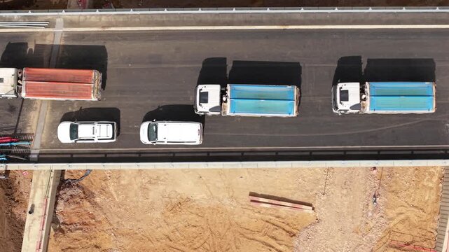 Aerial view of tipper trucks lined up in a queue waiting to deliver asphalt at a highway construction site in Bedfordshire, UK