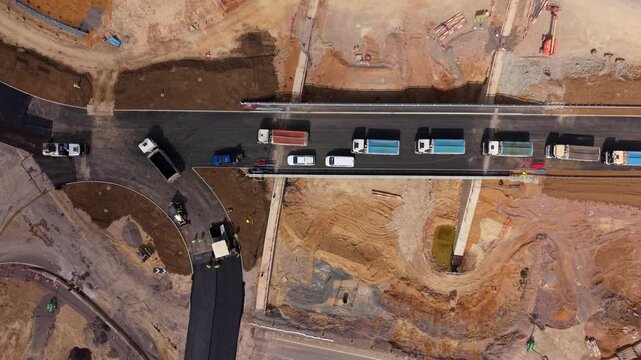 Aerial view of tipper trucks lined up in a queue waiting to deliver asphalt at a highway construction site in Bedfordshire, UK