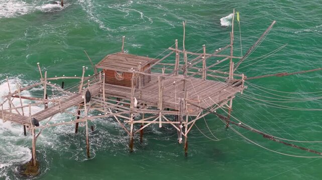 Trabocco Costa dei Trabocchi Abruzzo Italy top down drone flyback spider like wooden stilts ropes hut turquoise sea crashing waves ambient sound 4k video. Authentic Italian heritage