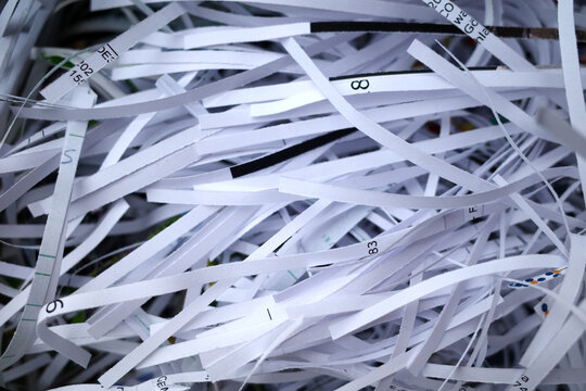 Thin strips of shredded white paper are tangled in a chaotic pile. Each strip features printed text and numbers. Shredding of paper is used for secure disposal of sensitive information.