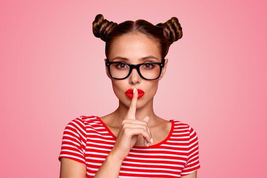 Shh! Portrait of attractive mysterious girl in glasses gesturing silence sign with forefinger red pout lips looking at camera isolated on red background