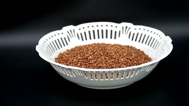 Roasted Buckwheat Groats in a Decorative White Ceramic Bowl on a Black Background