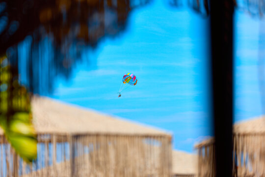 Parasailer flying over beach huts against a bright blue sky