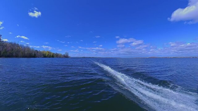 Boat wake foaming at water from outboard motor rear view. Waves from the outboard engine at high speed boat. Blue sky and clouds during sunny summer.  Wave from the boat moving. White foam from waves