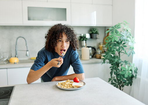 A teenage person sits at a kitchen table eating scrambled eggs and toast in the morning light. The casual, candid scene highlights a simple home breakfast routine and everyday lifestyle, with natural 