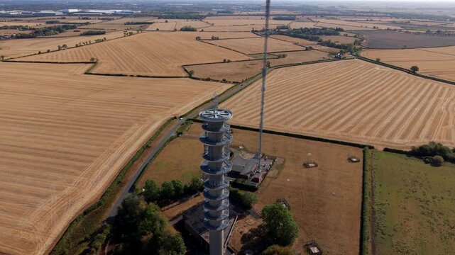 Detailed aerial view of steel transmission tower spire and radio frequency broadcast gear above parched English countryside