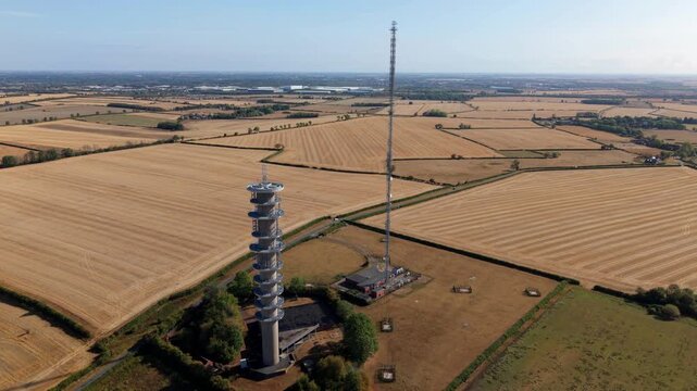 Detailed aerial view of steel transmission tower spire and radio frequency broadcast gear above parched English countryside