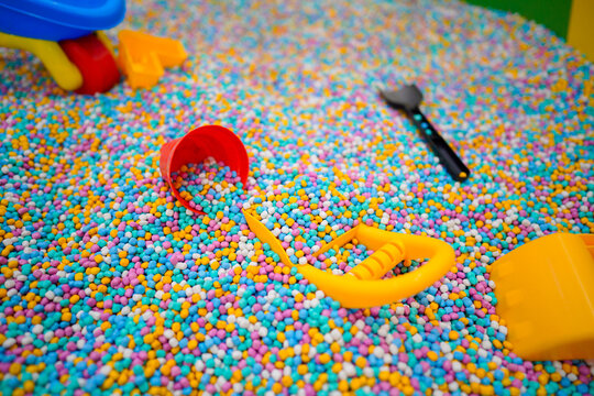Various colorful plastic toys and shovels scattered in a sensory pit filled with multi colored foam beads at an indoor kids playground.