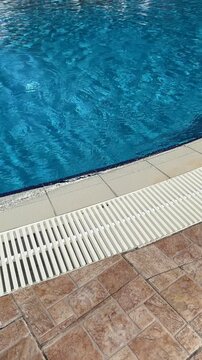 Pool edge tiled with slip-resistant ceramic or porcelain tiles, often bullnosed for safety, surrounding vibrant blue water in a resort or residential setting.