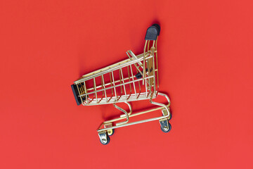 Golden empty shopping cart on red background © Firn