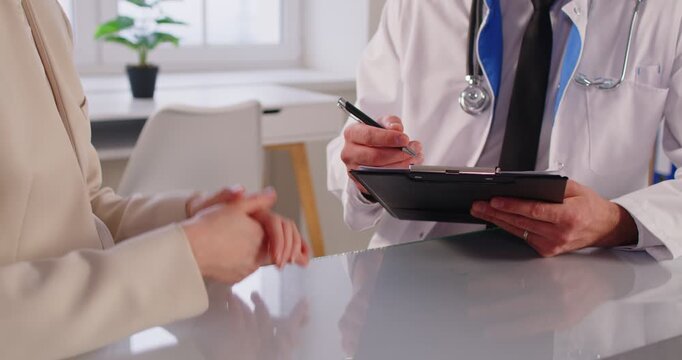 Cropped view of young female patient visiting doctor in medical clinic. Close up of physician consulting woman case, listening complaints and discussing treatment plan after examination in hospital.