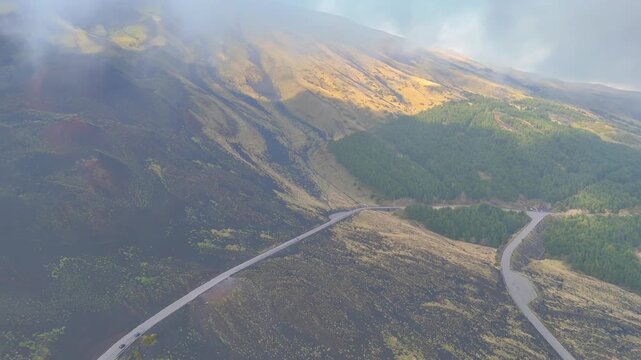 Aerial drone view of winding mountain road in pine forest under dramatic storm clouds on Mount Etna Sicily