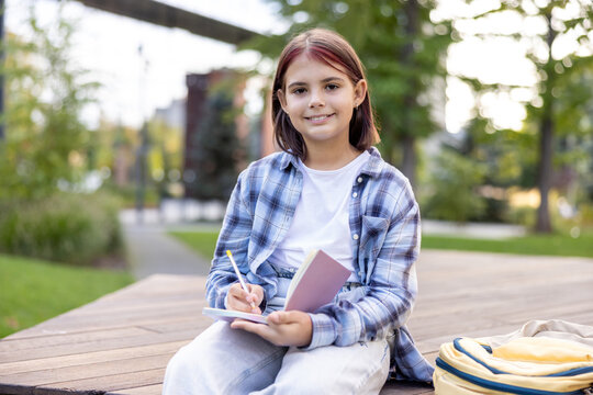 Student girl writing in notebook outdoors, enjoying park learning