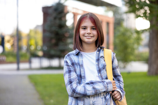 Happy schoolgirl standing outdoors carrying backpack smiling