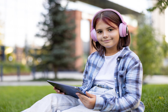 Young girl learning outdoors using tablet and headphones
