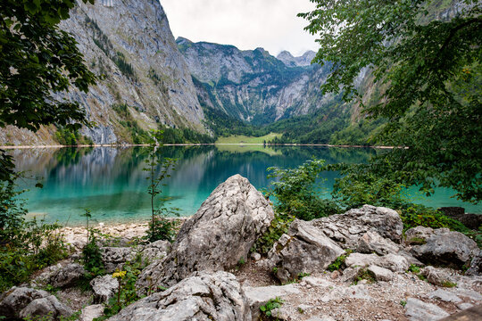 Serene alpine lake reflecting steep wooded mountains with rocky foreground in Bavaria Germany