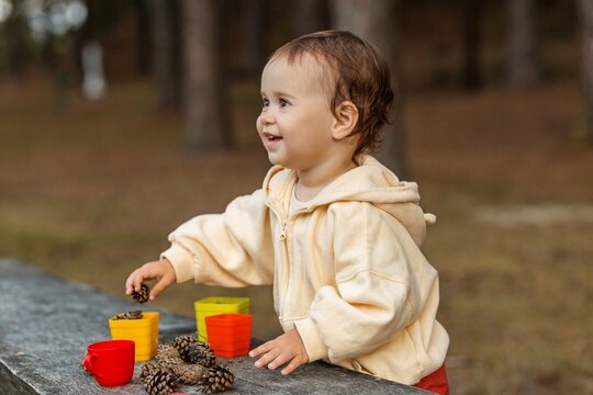 Toddler laughing joyfully while playing with pinecones outdoorssmil