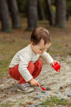Toddler squatting to scoop sand with spoon and cup