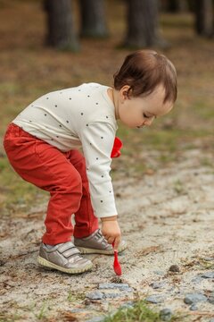 Toddler exploring ground outdoors with spoon during sensory play