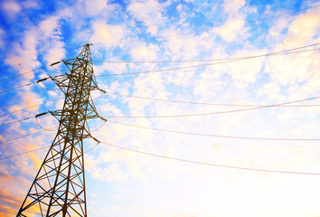 Obraz premium Silhouette of electricity pylon against blue sky with scattered clouds and warm golden hour lighting