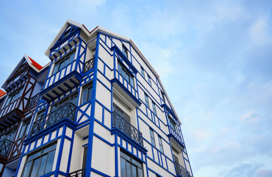 White building with blue timber framing and red roof under clear sky, low angle view showing architectural detail and balconies